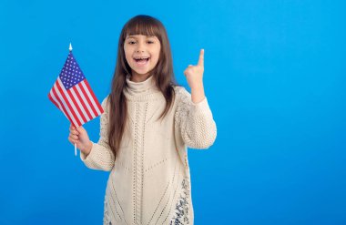 İyi fikir! ABD bayrağı ile küçük mutlu kız mavi bir arka planda bir parmak puan yukarı gösterir.