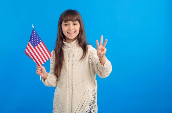 Malá Šťastná Dívka Vlajkou Usa Ukazuje Tři Prsty Stojící Modrém — Stock fotografie