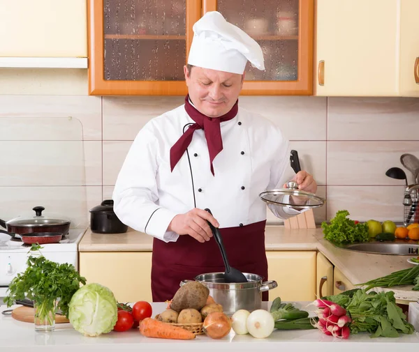 Mature male cook in the kitchen prepares dietary food from vegetables. Make a lean dish.