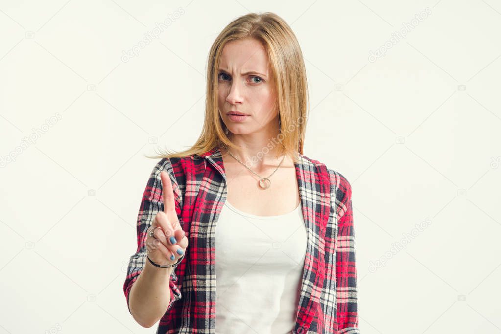 Serious woman shows a finger gesture attention or stop standing on a light background.
