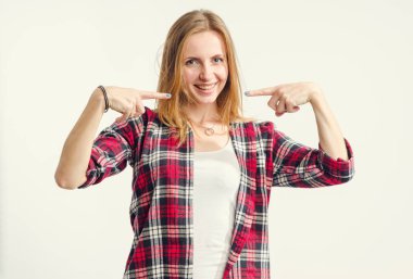 Güzel mutlu genç kadın hafif bir arka plan üzerinde dururken gülümsemesi ve dişleri üzerinde parmak gösterir.