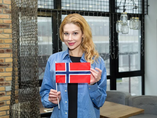 Norveç bayrağı taşıyan genç bir İskandinav kadın ofiste dikiliyor. Yurtdışında okuyun ve çalışın. Norveççe öğren.
