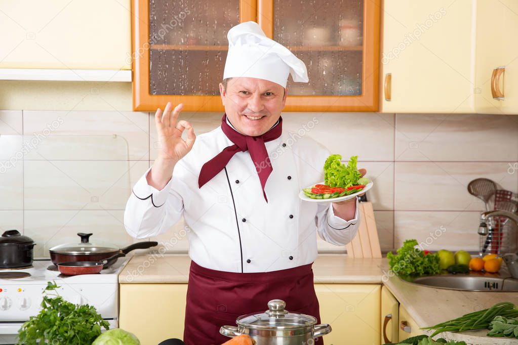 Portrait of a male cook in the kitchen. Male chef cooks food. Show gesture okay.