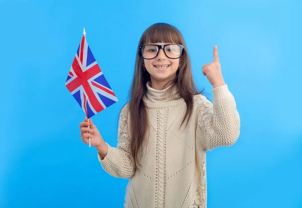 带着英国国旗的小女孩在蓝色背景上竖起大拇指 女学生在国外学习 学习英语 — 图库照片