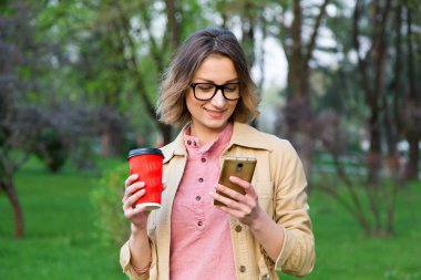 Çevrimiçi sohbet. Gözlüklü genç kadın akıllı telefondaki mesajları okur ve kahve içer.