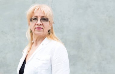Gözlüklü mutlu olgun kadın portresi, yaş 60 gri duvara karşı.