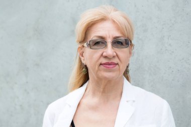 Gözlüklü mutlu olgun kadının yakın portresi, yaş 60 gri duvara karşı.