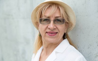 Gözlük ve şapka ile mutlu bir olgun kadının yakın portresi.