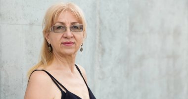 Gözlüklü mutlu olgun kadının yakın portresi, yaş 55 veya 60 yıl gri duvara karşı.