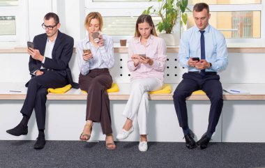 Ofiste oturan iş insanları grubu akıllı telefonlarına bakıyor. Kahve molası. Toplantı bekleniyor.