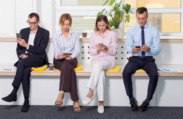 坐在办公室里的一群商界人士正在查看他们的智能手机 咖啡休息 等待会议 — 图库照片