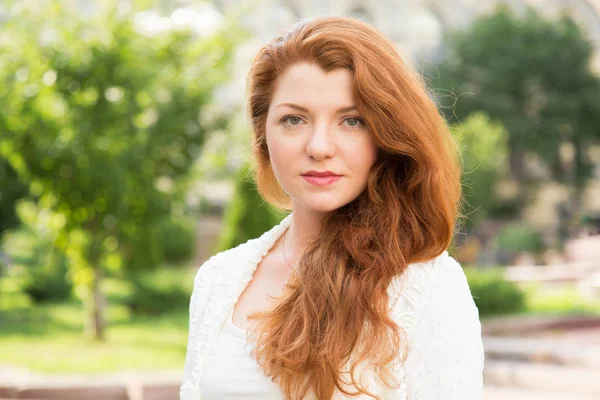 Bir yaz gününde yeşil ağaçların bir arka planda kırmızı saçlı bir kadının portresi.