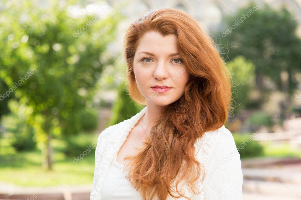 Portrait of a red-haired woman on a background of green trees on a summer day.