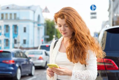 Kırmızı saç kadın yürüyüş ve bir şehir sokakta akıllı telefon kullanarak.