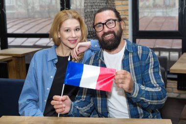 Couple, bearded man in glasses and blond woman with France flag sitting in office.
