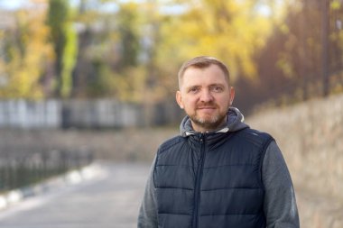 Sakallı orta yaşlı bir adamın portresi Sonbahar şehri sokaklarının arka planında.