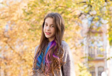 Saçında çok renkli örgüler olan genç bir kızın portresi bir sonbahar parkının arka planına karşı..