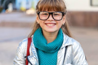 Cheerful girl of 9 - 10 years in glasses against the background of the city. Happy child.