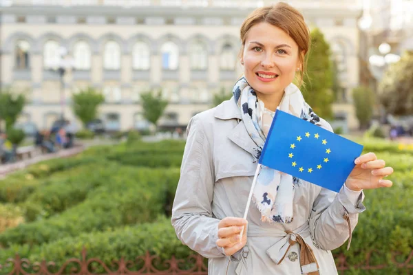 Middle-aged woman with the flag of the European Union on a background of the park and the city.