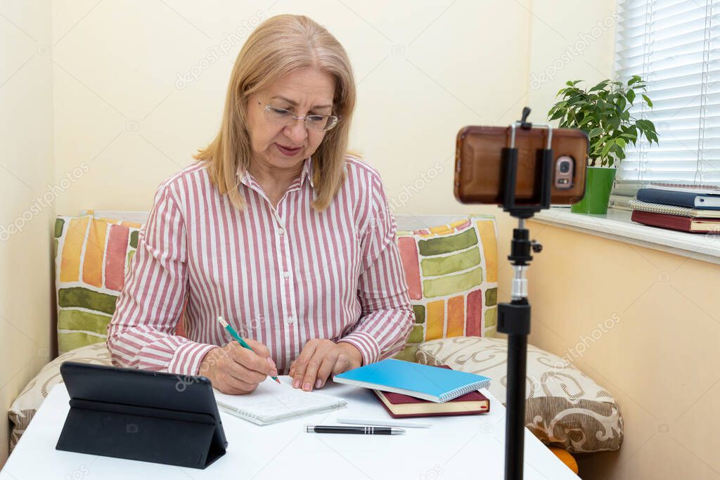 Adult woman looks in a smartphone and makes notes, online training.