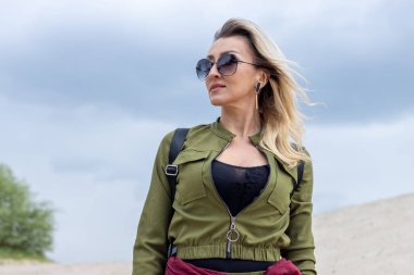 Mavi bir arka planda, güneş gözlüklü ve askeri tarzda giyinmiş yetişkin bir kadının portresi..