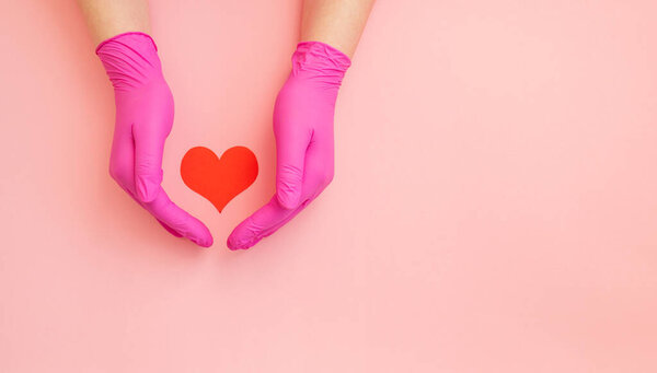 Крупным планом руки в розовой защитной держать красное сердце. Концепция кардиологии
.