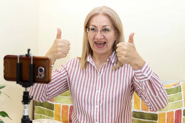 熟女60歳の女がブログ用のスマホカメラ動画に記録しています 親指を立てる ジェスチャー オンライン教育 — ストック写真