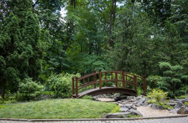 Yeşil ağaçlı bahçe manzaralı bir park ve Asya tarzı bir köprü..