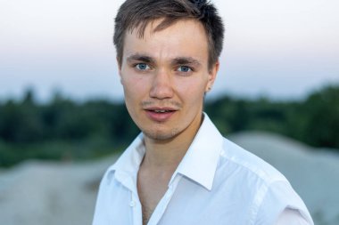 Beyaz tişörtlü yakışıklı bir adamın portresi günbatımının arka planına karşı..