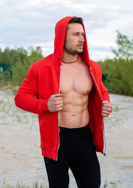 Muscular man in a red sports jacket is engaged in fitness in nature.