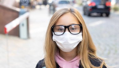 Gözlüklü ve koruyucu maskeli genç bir kızın portresi yol boyunca arabalarla geziyor..