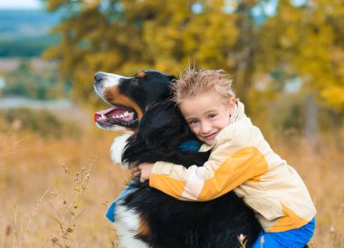 sevimli çocuk onun köpek yürümek-den geçerek sonbahar çayır nın Sennenhun sarılma sarı ceketli