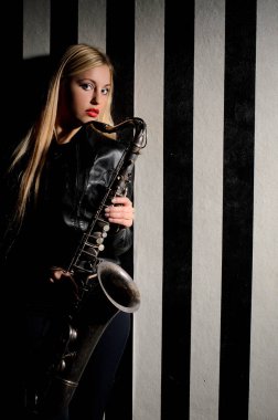 Girl with saxophone in contrast illumination stands near wall with white and black stripes clipart