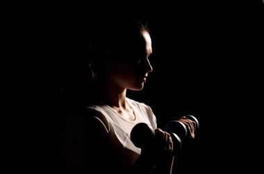 Tamamen siyah bir arka plan üzerinde spor için kız elinde dumbbells ile giriyor