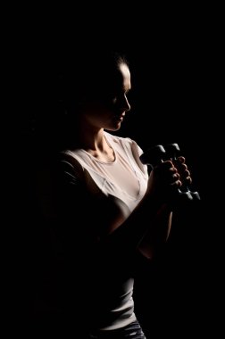 Tamamen siyah bir arka plan üzerinde spor için kız elinde dumbbells ile giriyor