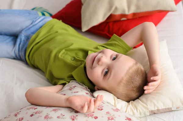 boy lying on his back in a green T-shirt. On the bed of colorful pillows