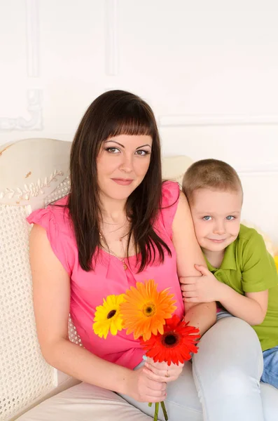 妈妈在沙发上带着鲜花 抱着儿子和妈妈的微笑 — 图库照片