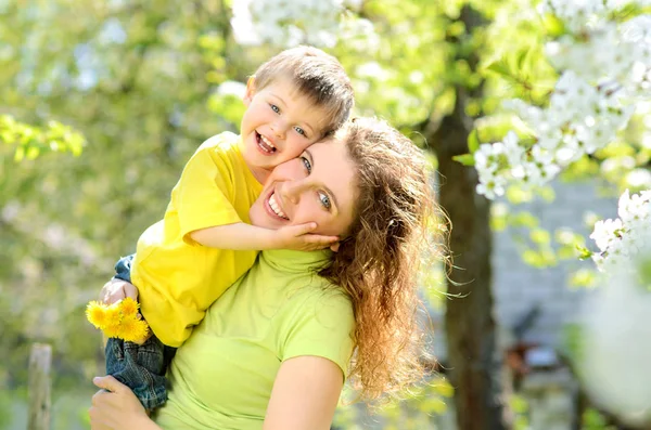 Yemyeşil bahar bahçe Apple annesinin kollarında mutlu gülümseyen küçük çocuk