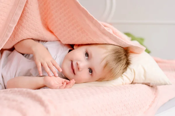 Blond Chłopiec Leżąc Łóżku Pod Różowym Kocem Białą Poduszkę — Zdjęcie stockowe
