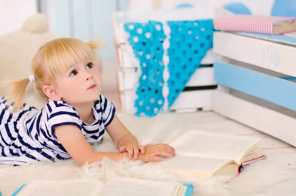 クマのぬいぐるみの横にある本を床に横になっている金髪の女の子 — ストック写真