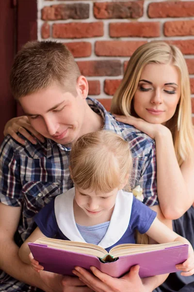 Familia Leyendo Libro Con Hija Sobre Fondo Una Pared Ladrillo —  Fotos de Stock