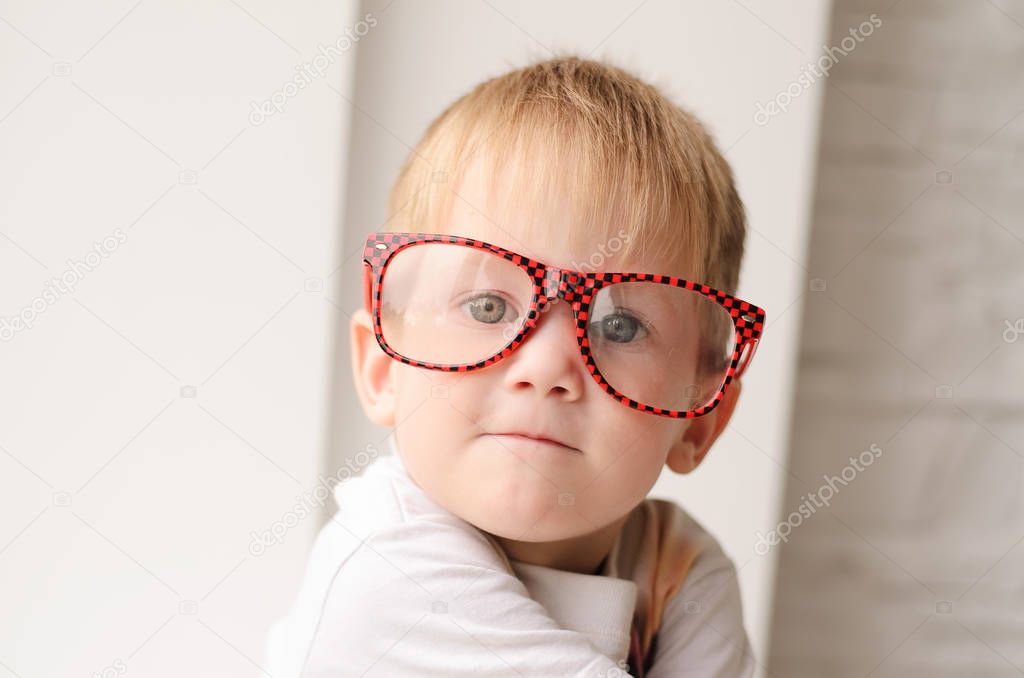 Blond boy in red glasses close up sitting on a background of a white brick wall