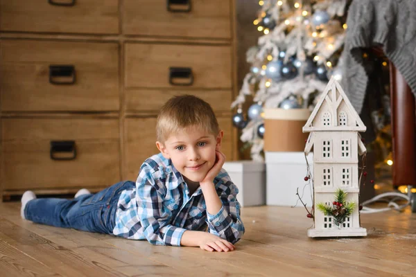 Chlapec Leží Dřevěné Podlaze Blízkosti Domečku Pozadí Vánočního Stromku Dárkovými — Stock fotografie