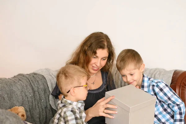 幸せと愛情のあるお母さん 子供たちは大きな灰色のギフトボックスで驚きを示しています 部屋のソファに座って — ストック写真