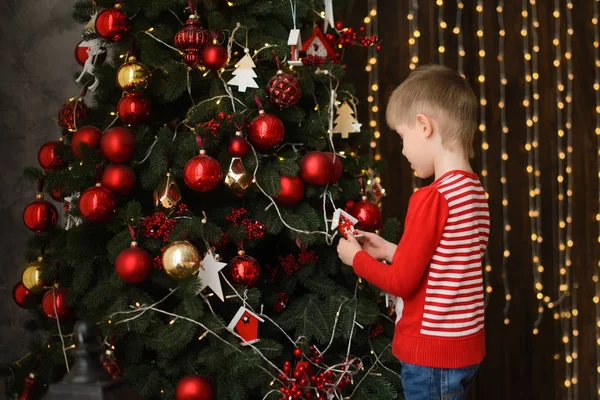 Pojke Tröja Dekorerar Julgran Med Röda Bollar Mot Bakgrund Trävägg — Stockfoto