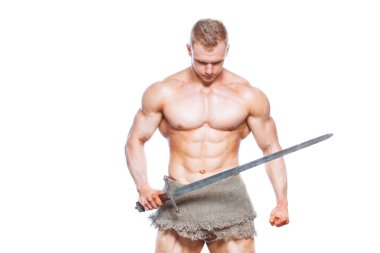 Vücut geliştirmeci adam beyaz arka plan üzerinde izole bir kılıç ile poz. Ciddi gömleksiz adam mascular vücudunu gösteren.