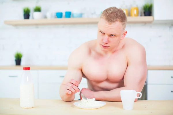 Homem muscular com um tronco nu na cozinha com leite e queijo cottage, o conceito de uma dieta saudável. Modo de vida atlético . — Fotografia de Stock