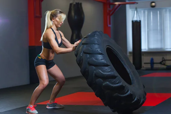 Apto atleta feminino exercitar-se com um pneu enorme, girando e transportar no ginásio. Crossfit mulher exercitando com pneu grande — Fotografia de Stock