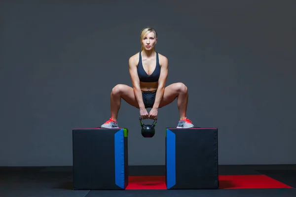 Жінка займається в спортзалі з вагою чайника, на кубиках — стокове фото
