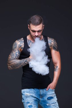 Vaper. Dövmeli kas bir gövde adamla koyu arka plan üzerinde elektronik sigara duman
